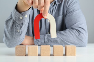 Photo of Man with magnet attracting wooden cubes at white table, closeup