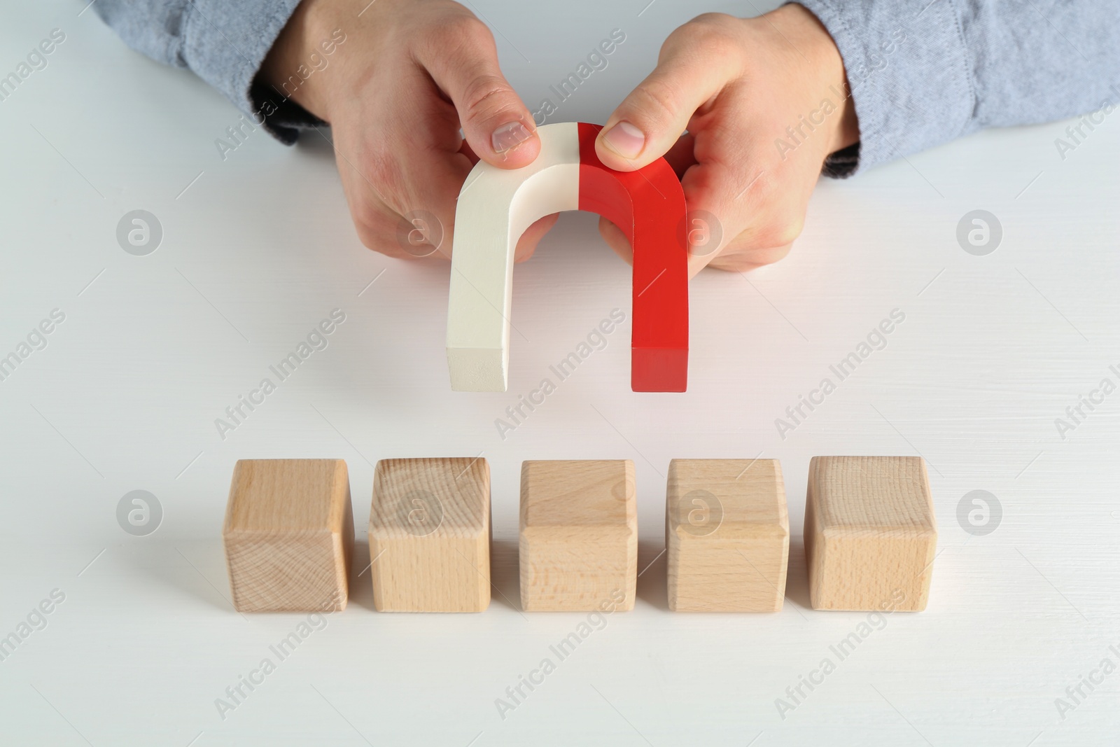 Photo of Man with magnet attracting wooden cubes at white table, closeup