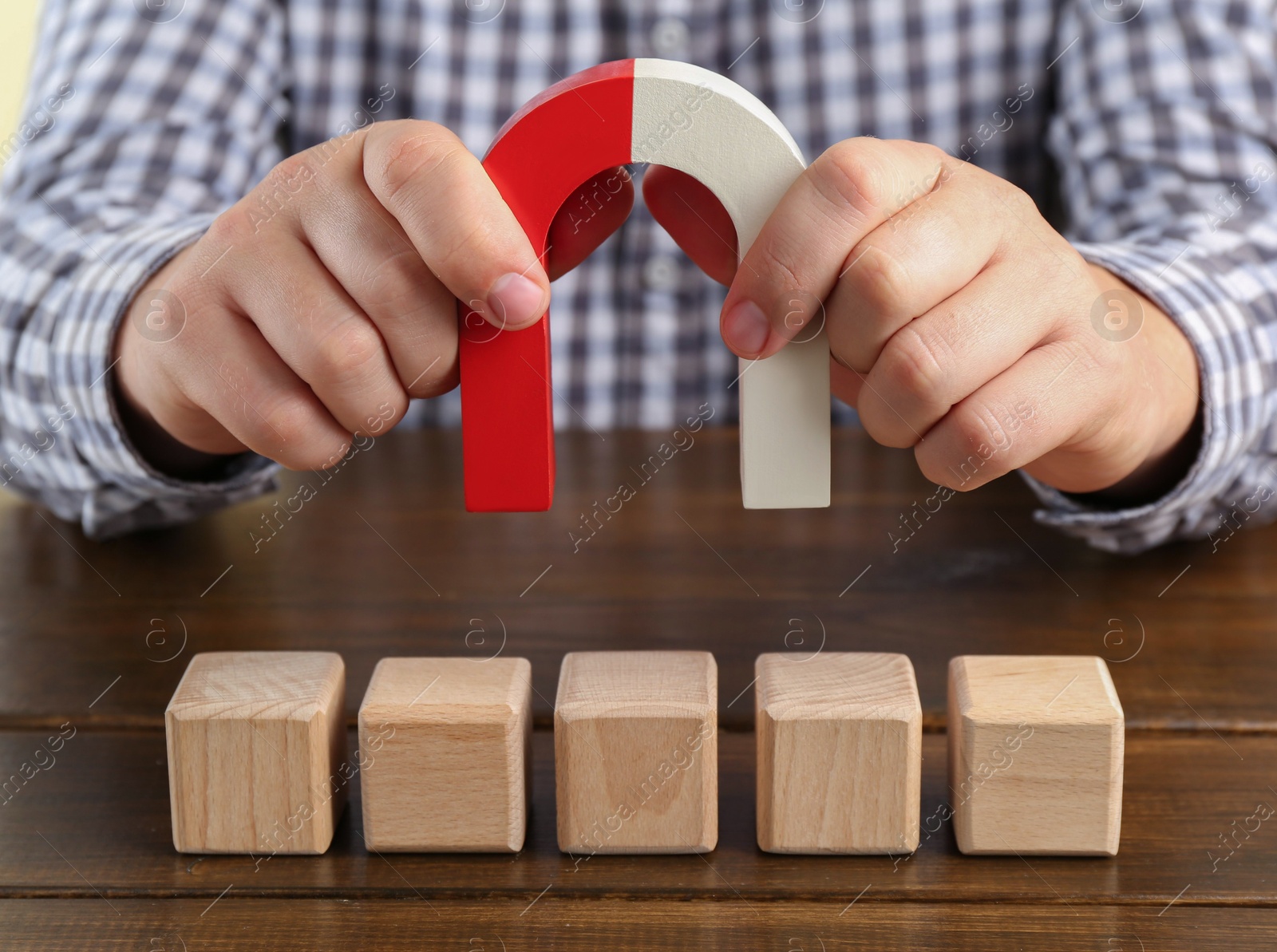 Photo of Man with magnet attracting cubes at wooden table, closeup