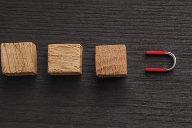 Photo of Magnet attracting cubes on black wooden table, flat lay