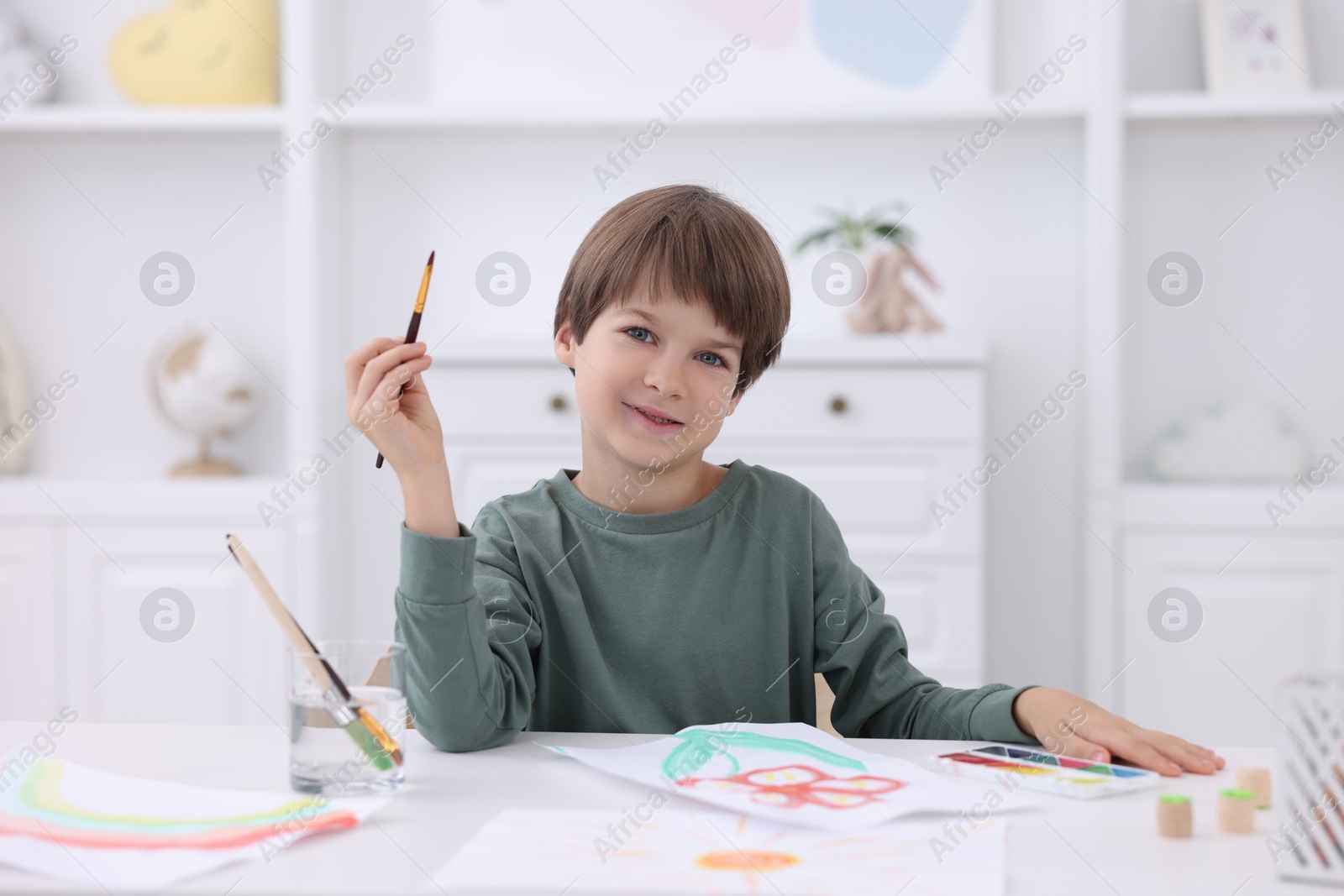 Photo of Cute boy drawing at white table in kindergarten