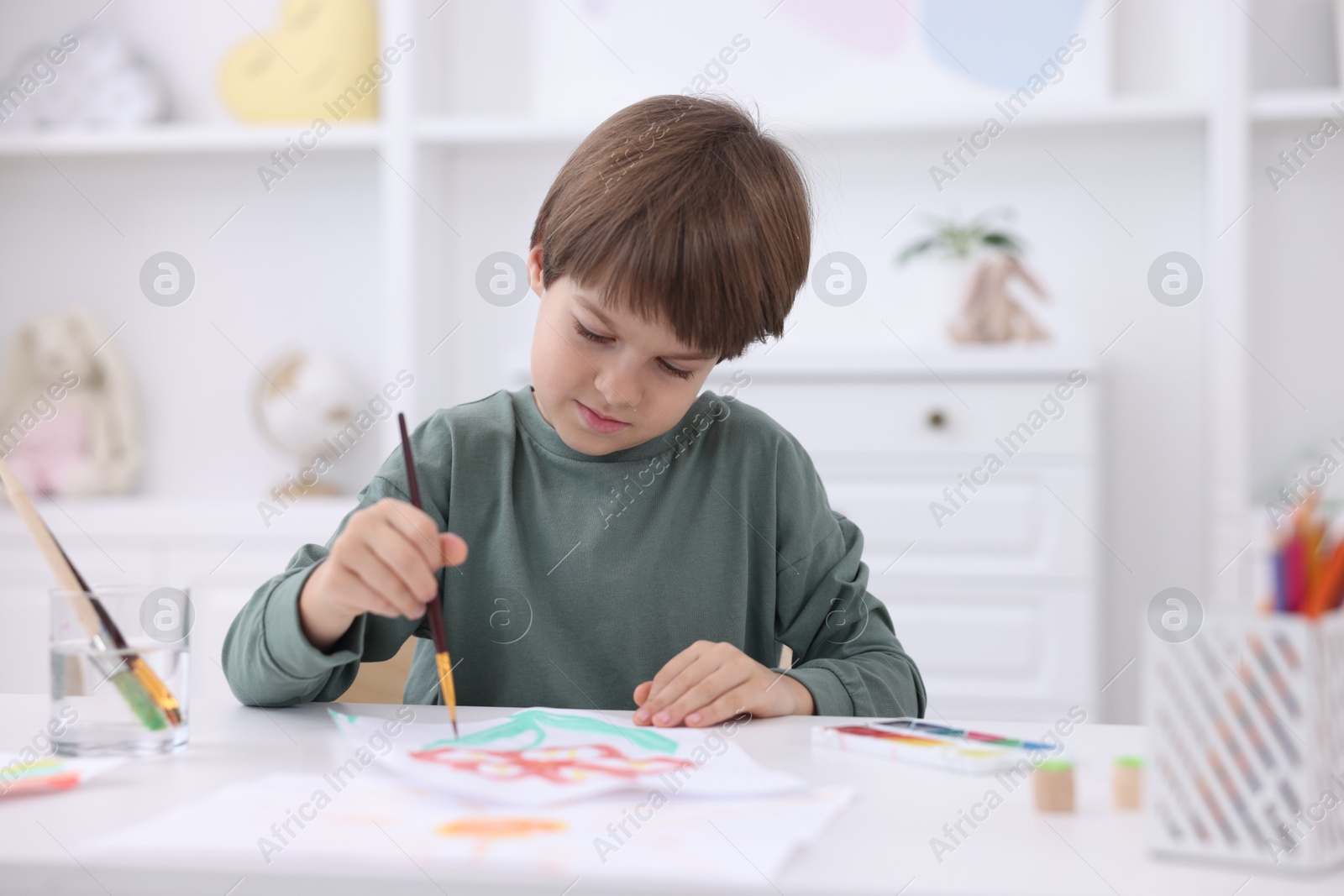 Photo of Cute boy drawing at white table in kindergarten