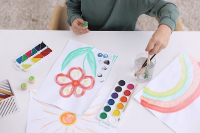 Photo of Little boy drawing at white table indoors, closeup