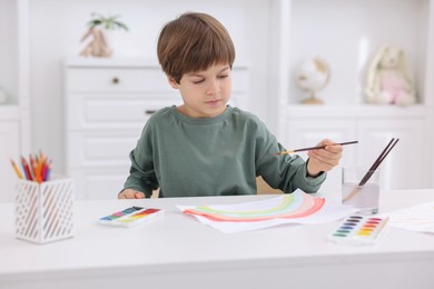 Photo of Cute boy drawing at white table in kindergarten