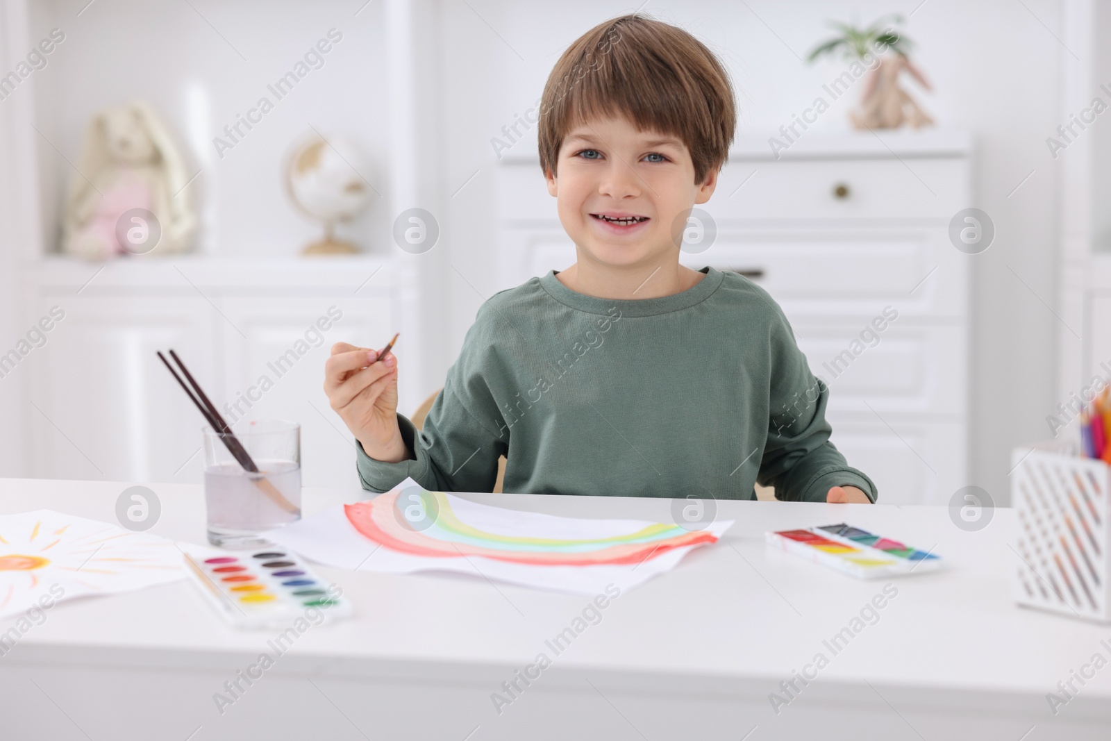 Photo of Happy boy drawing at white table in kindergarten