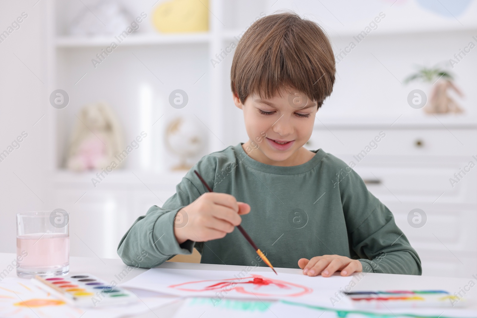 Photo of Cute boy drawing at white table in kindergarten