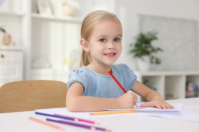 Photo of Portrait of smiling girl drawing at white table in kindergarten