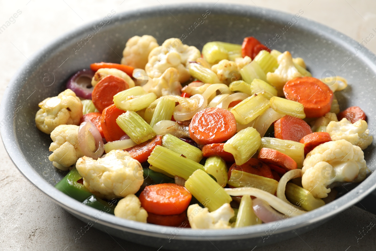 Photo of Frying pan with vegetables on light textured table, closeup