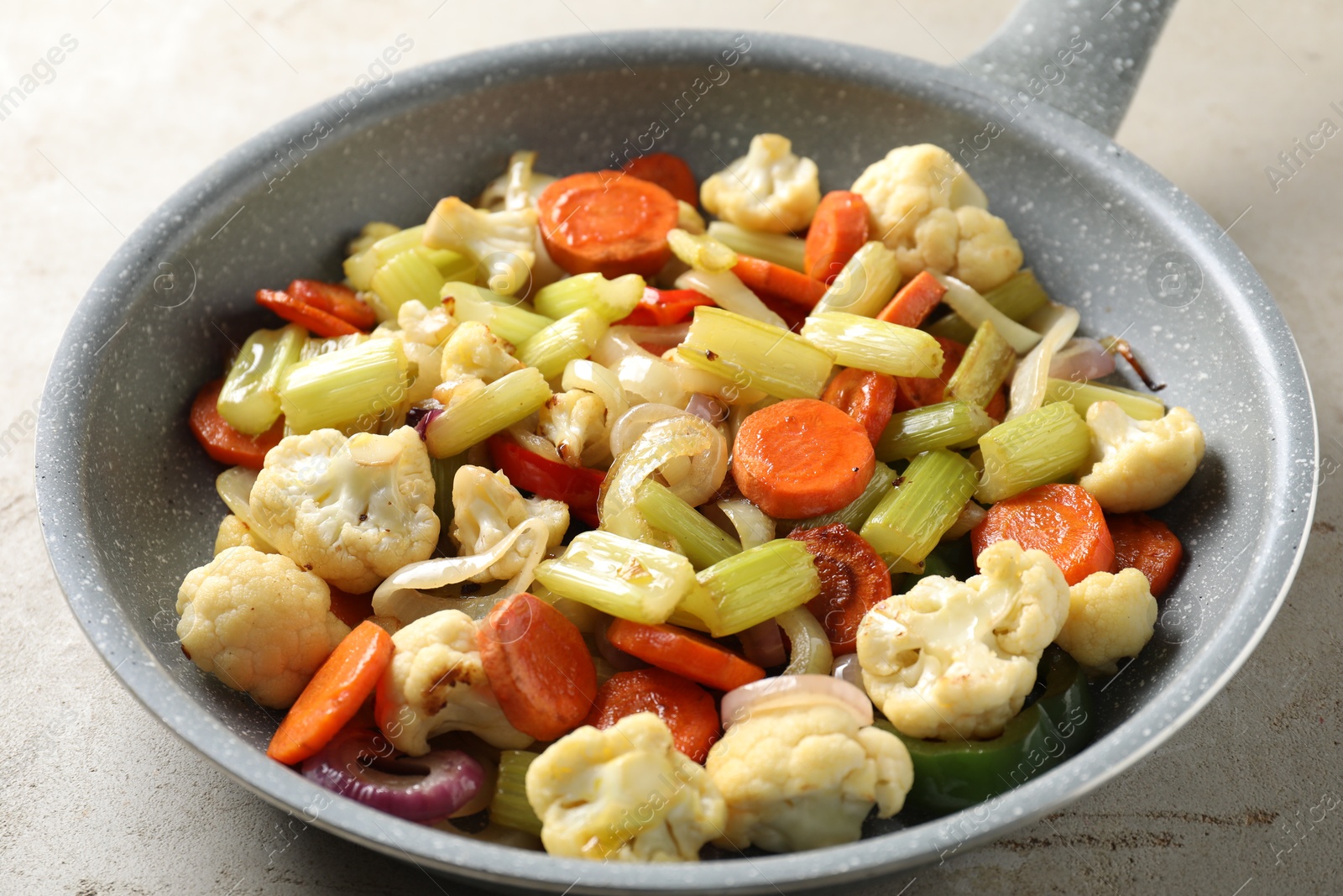 Photo of Frying pan with vegetables on light textured table, closeup