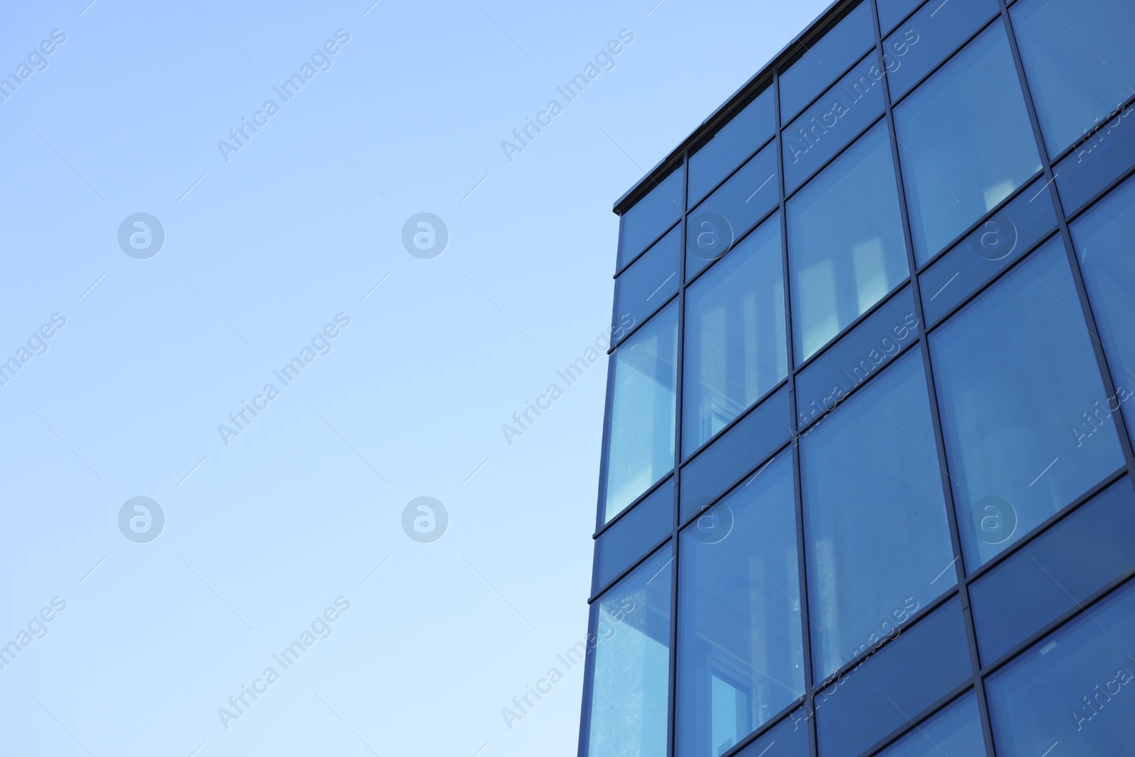 Photo of Exterior of modern building with many windows against light blue sky, low angle view. Space for text