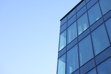 Exterior of modern building with many windows against light blue sky, low angle view. Space for text