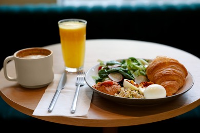 Photo of Tasty breakfast. Freshly baked croissant and salad served on wooden table in cafe