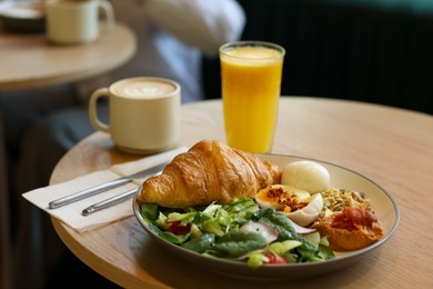 Photo of Tasty breakfast. Freshly baked croissant and salad served on wooden table in cafe, closeup