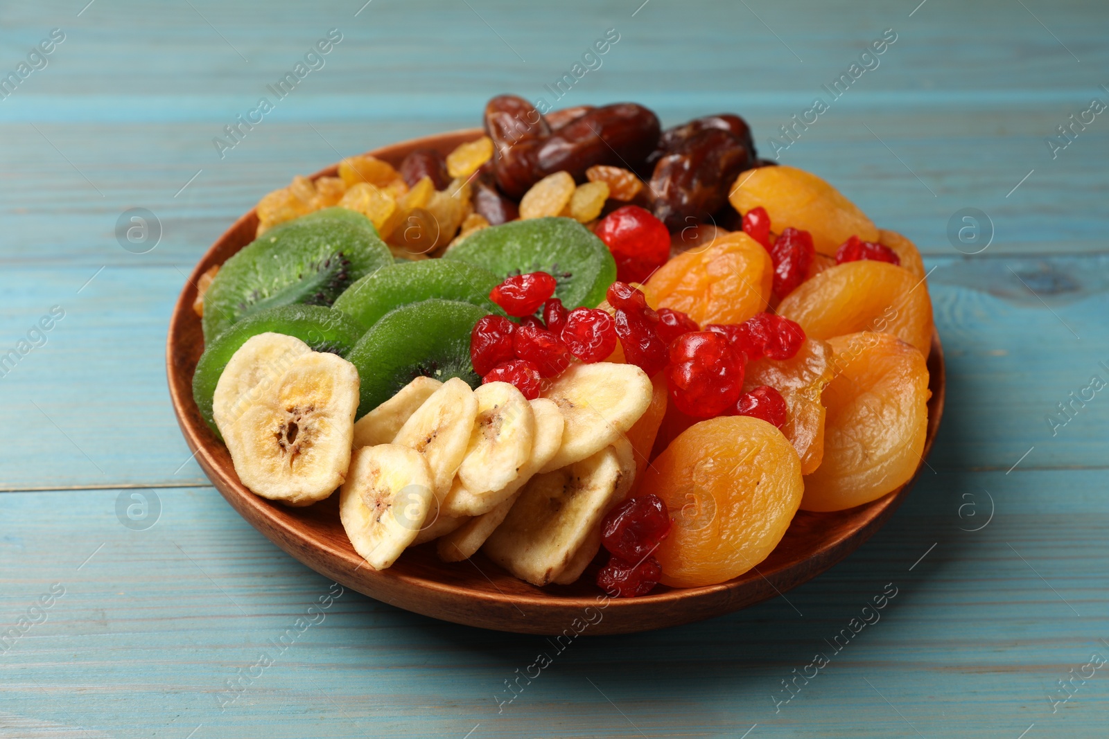 Photo of Mix of different dried fruits in bowl on blue wooden table, closeup