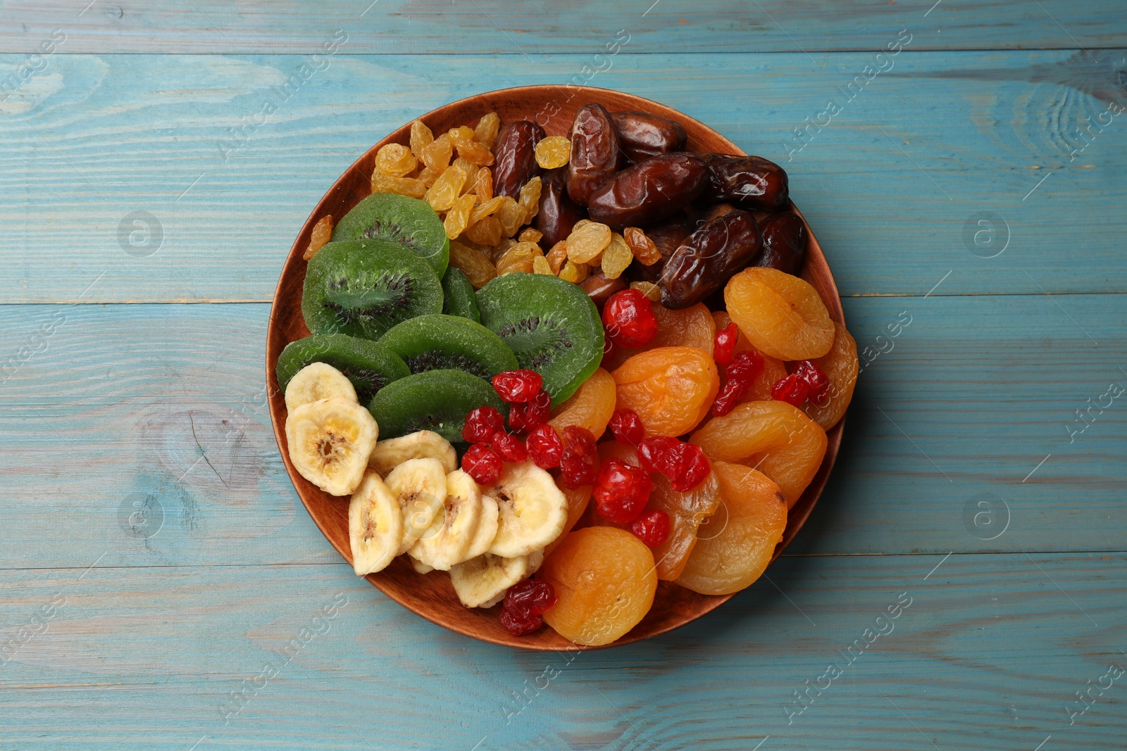 Photo of Mix of different dried fruits in bowl on blue wooden table, top view