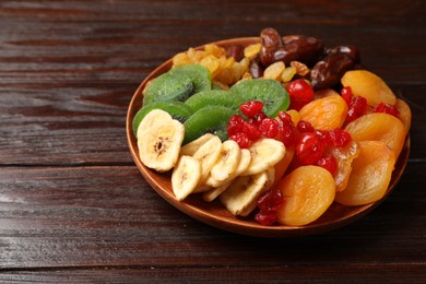 Photo of Mix of different dried fruits in bowl on wooden table, closeup