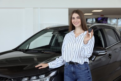 Photo of Happy young woman holding key near new black car in salon