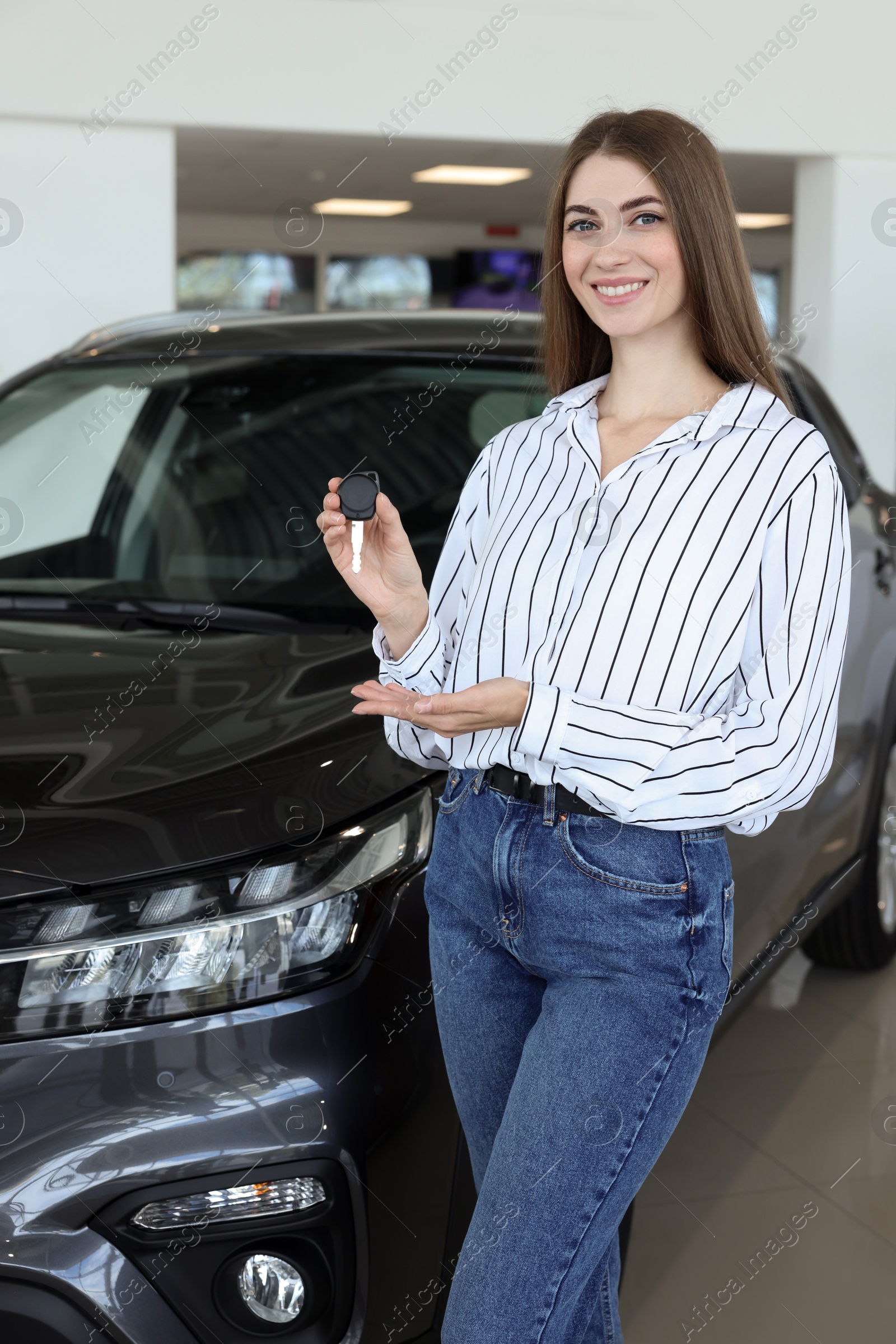 Photo of Happy young woman holding key near new black car in salon