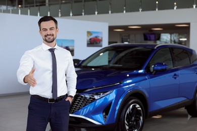 Photo of Happy salesman reaching for handshake with client near new blue car in salon