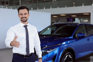 Photo of Happy salesman reaching for handshake with client near new blue car in salon