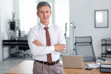 Portrait of smiling middle aged man with crossed arms in office