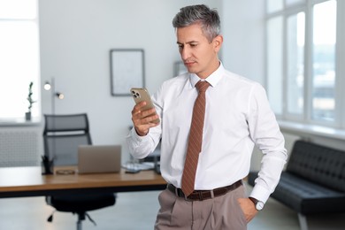 Photo of Middle aged man looking at smartphone in office