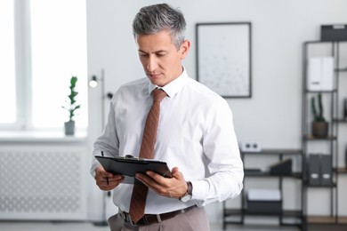 Photo of Middle aged man working with clipboard in office