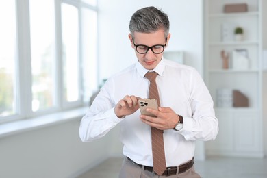 Middle aged man using smartphone in office. Space for text