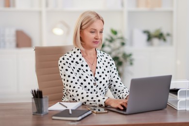 Middle aged woman working with laptop at table in office