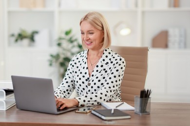 Smiling middle aged woman working with laptop at table in office