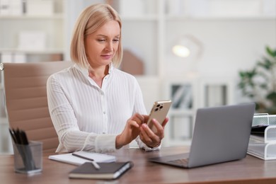 Photo of Middle aged woman using smartphone at table in office