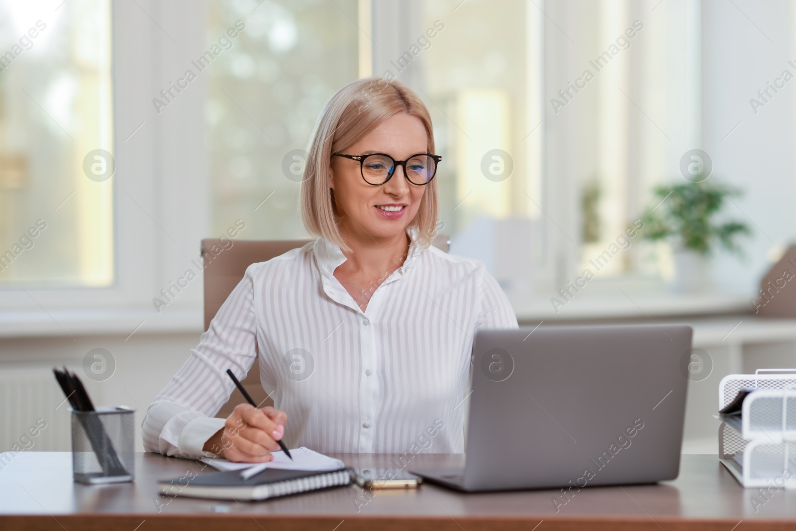 Photo of Smiling middle aged woman working with laptop at table in office