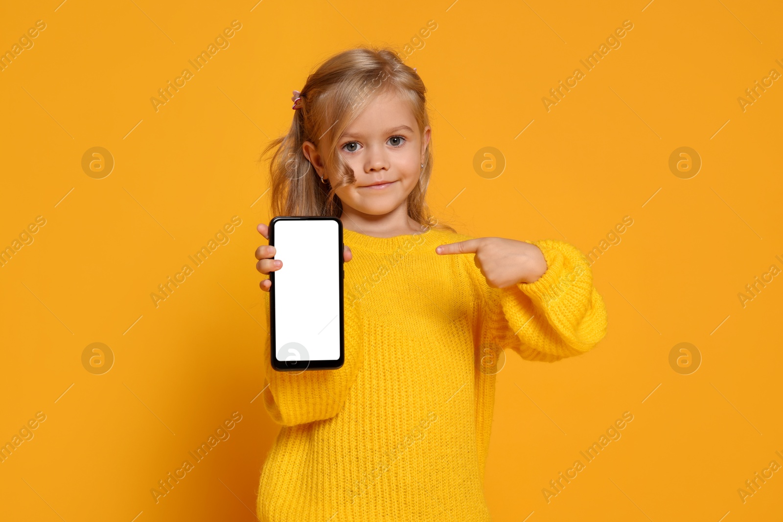 Photo of Cute little girl with smartphone against orange background