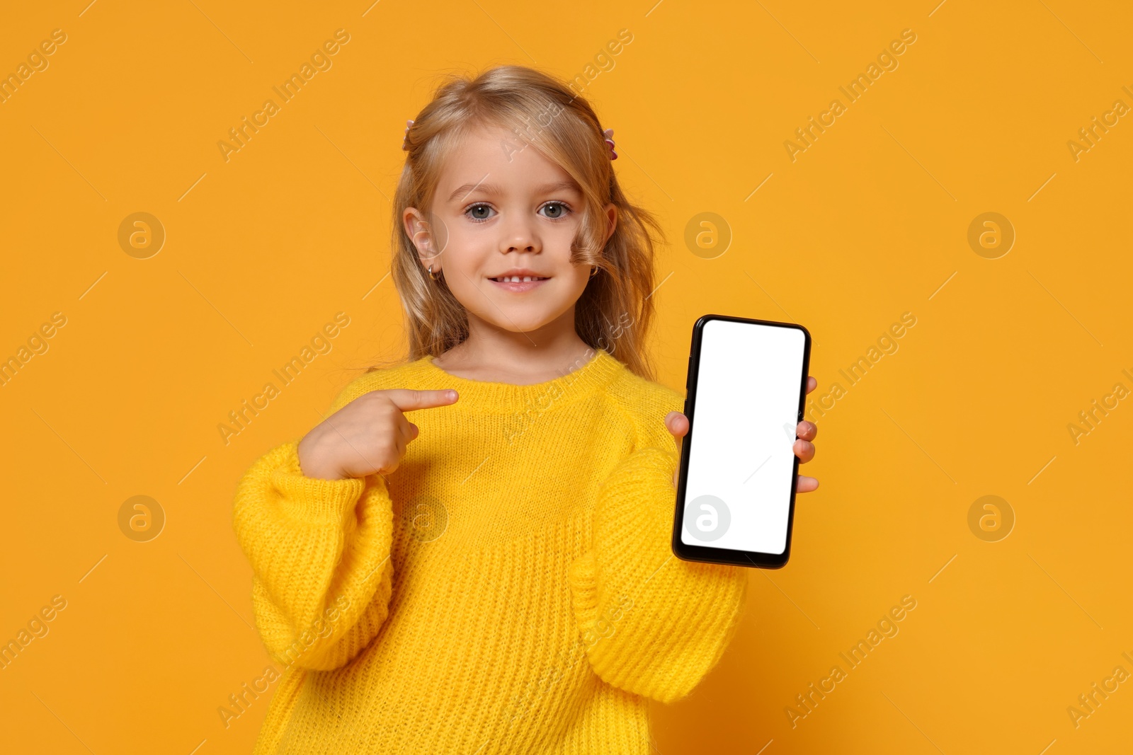 Photo of Cute little girl with smartphone against orange background