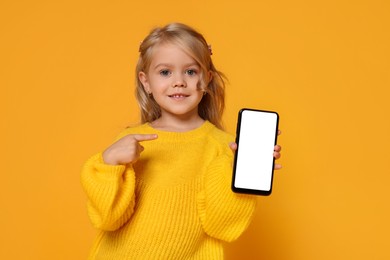 Photo of Cute little girl with smartphone against orange background