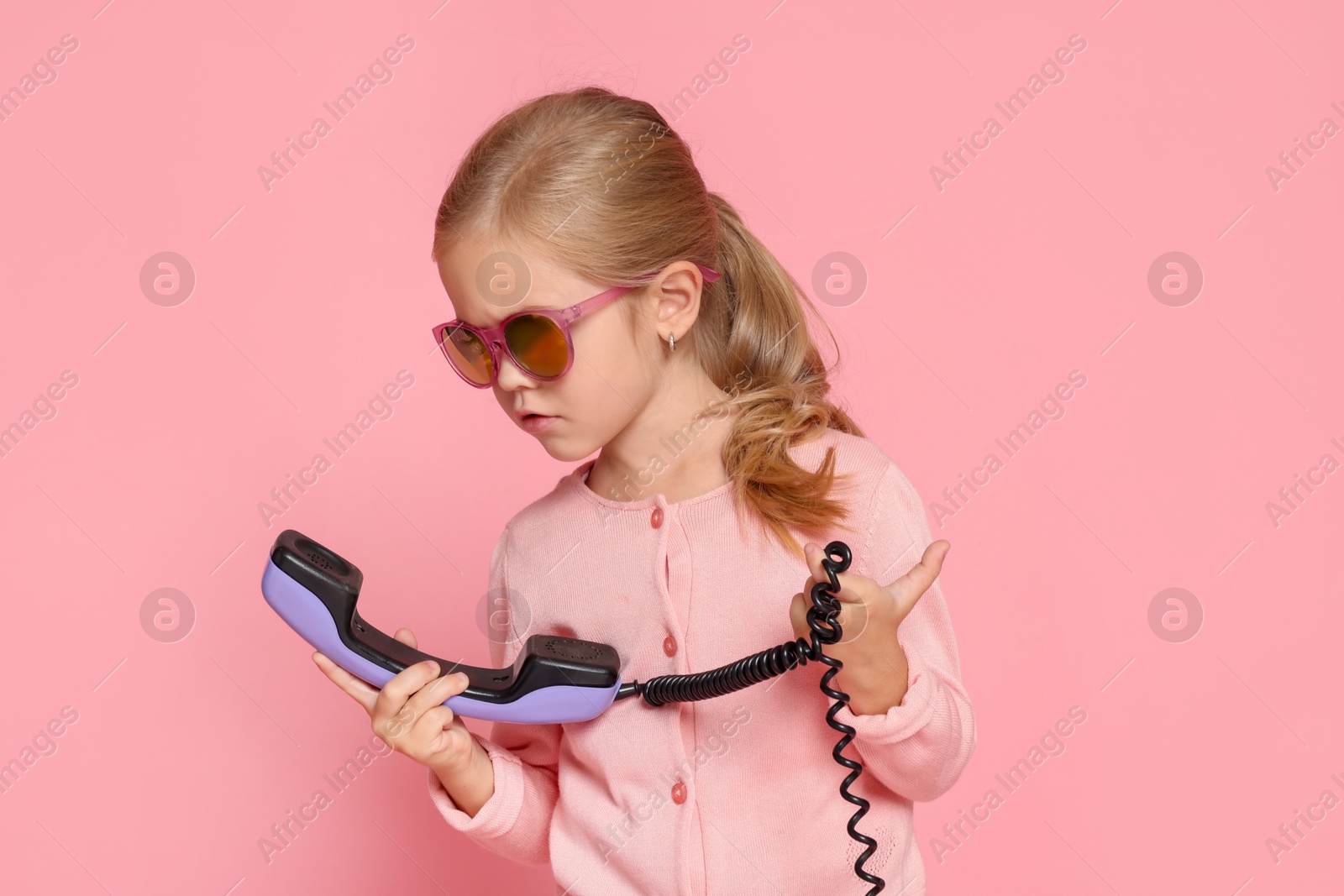 Photo of Cute little girl with handset of telephone on pink background