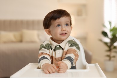 Photo of Cute little kid sitting in high chair at home