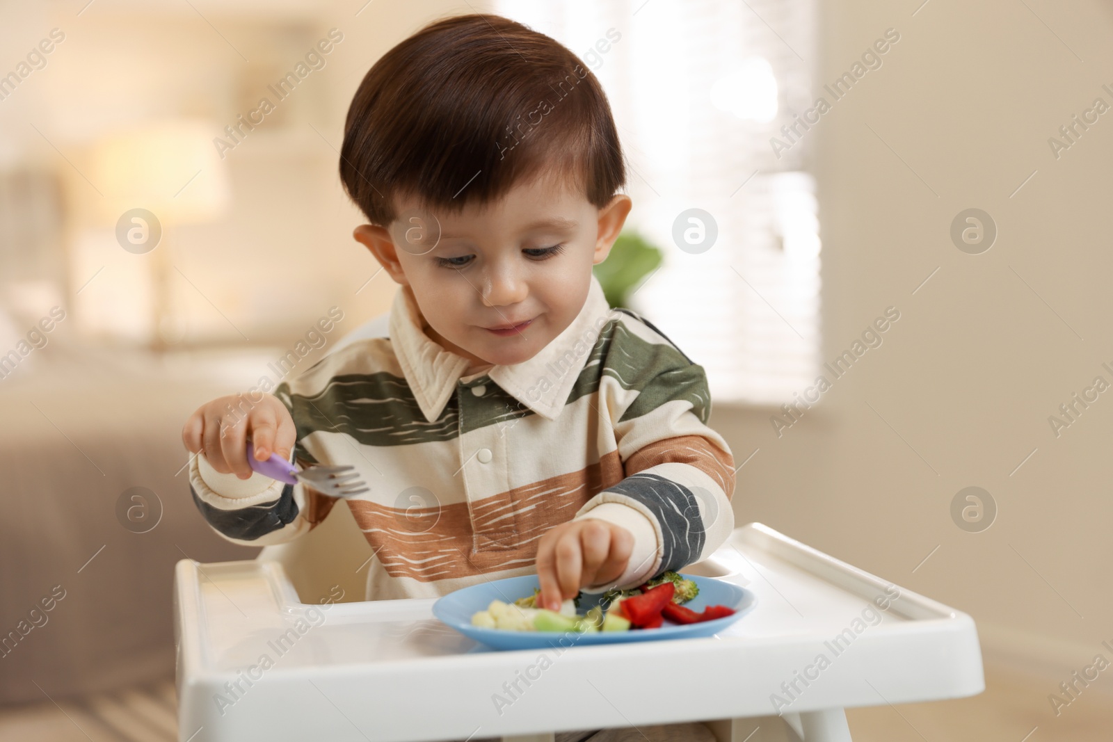 Photo of Cute little baby eating healthy food in high chair at home