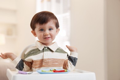 Photo of Cute little baby eating healthy food in high chair at home