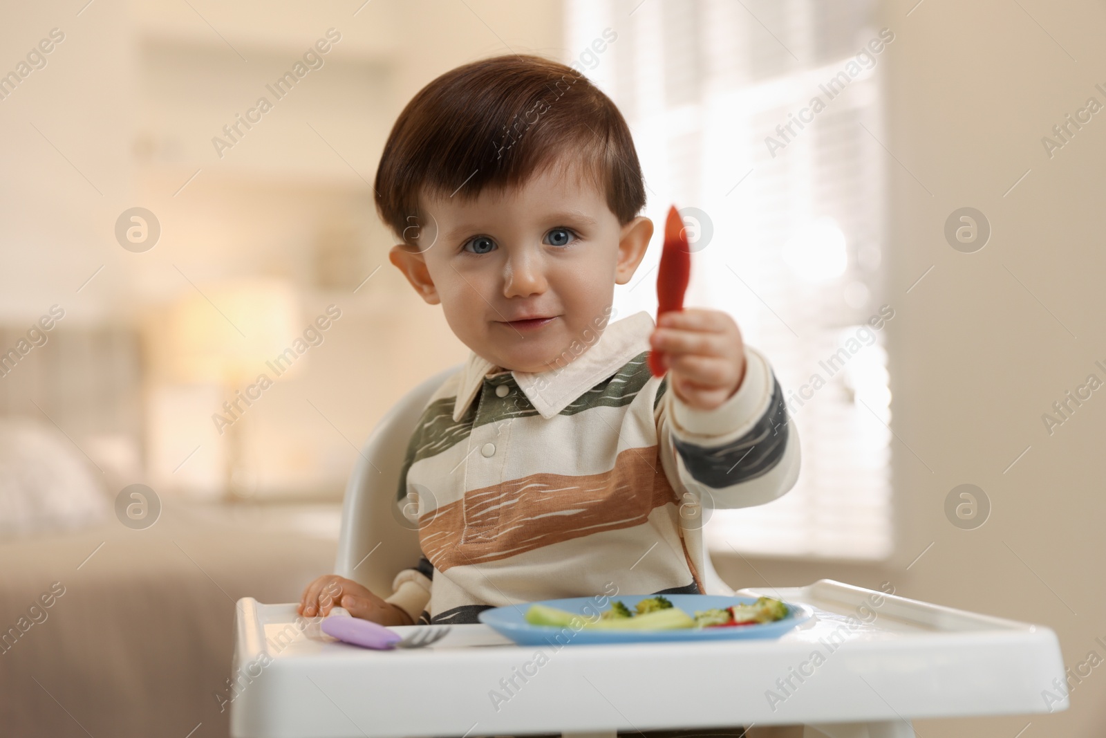 Photo of Cute little baby eating healthy food in high chair at home