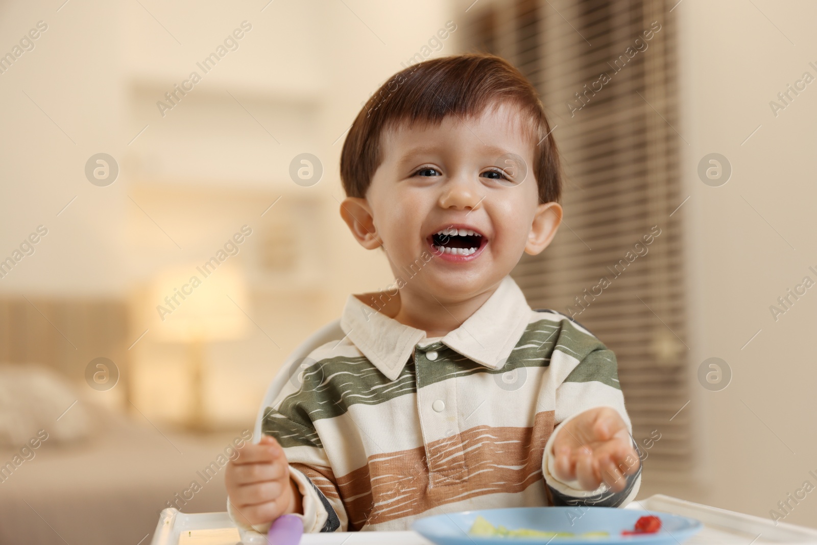 Photo of Cute little baby eating healthy food in high chair at home