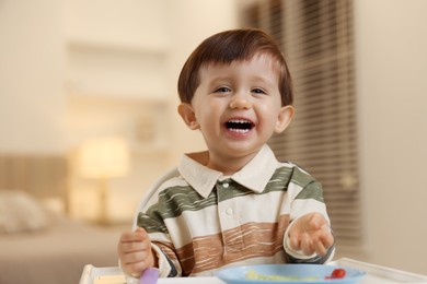 Photo of Cute little baby eating healthy food in high chair at home