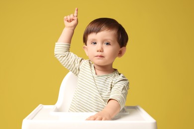 Photo of Cute little kid sitting in high chair on yellow background