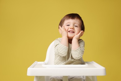 Photo of Cute little kid sitting in high chair on yellow background