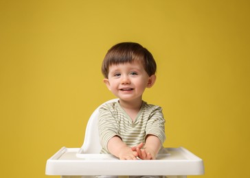 Photo of Cute little kid sitting in high chair on yellow background