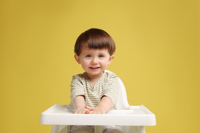 Photo of Cute little kid sitting in high chair on yellow background