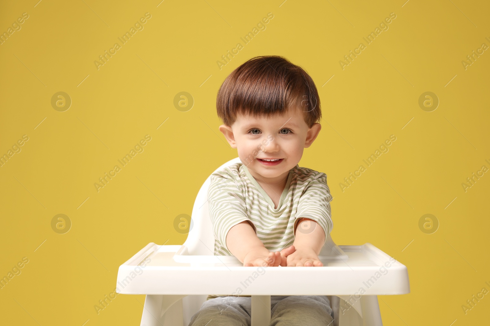 Photo of Cute little kid sitting in high chair on yellow background