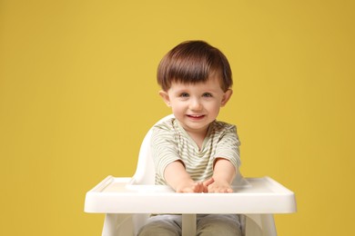 Photo of Cute little kid sitting in high chair on yellow background