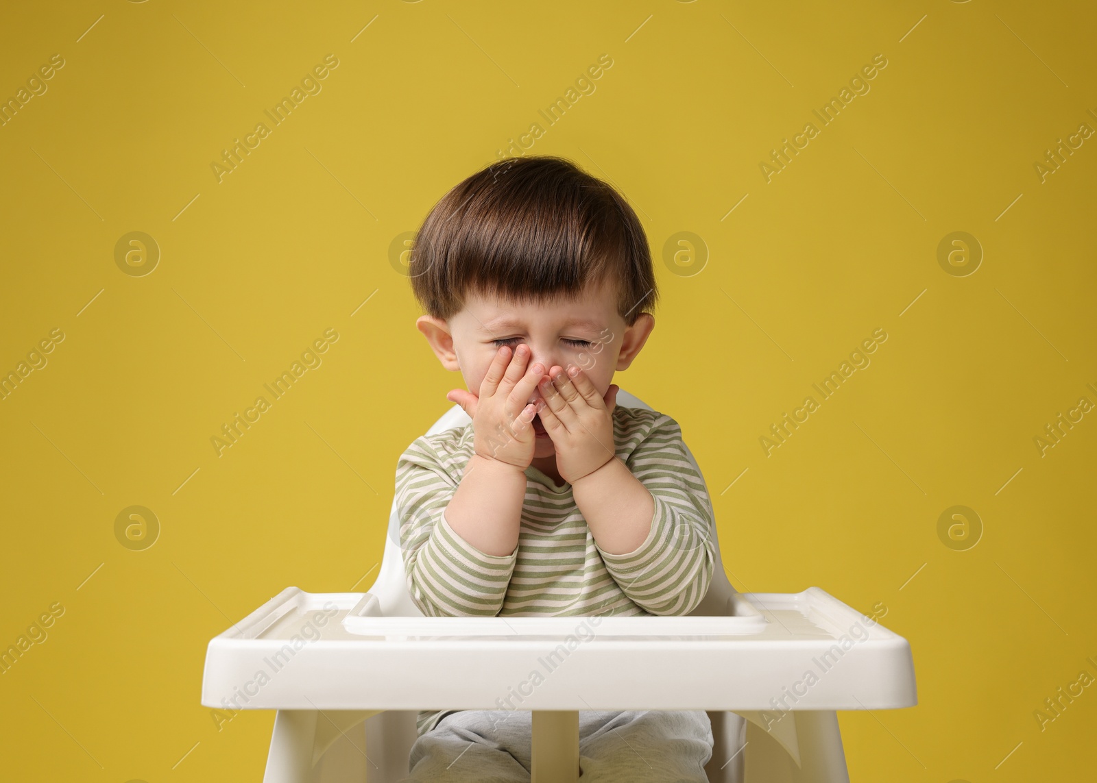 Photo of Cute little kid sitting in high chair on yellow background