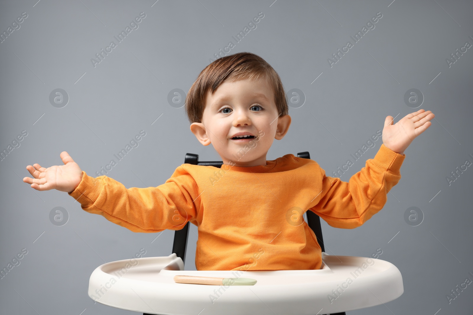 Photo of Cute little kid with spoon sitting in high chair on light grey background